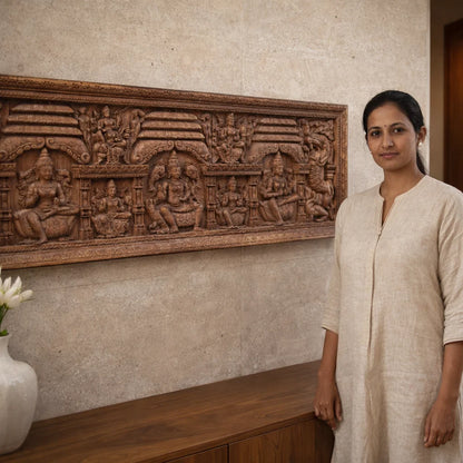 Woman standing next to a decorative wall panel with carvings in a room.

